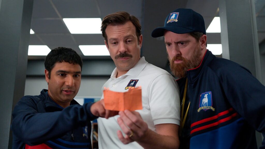 Nate, Ted Lasso and Coach Beard look at a recipe together in Ted Lasso. 